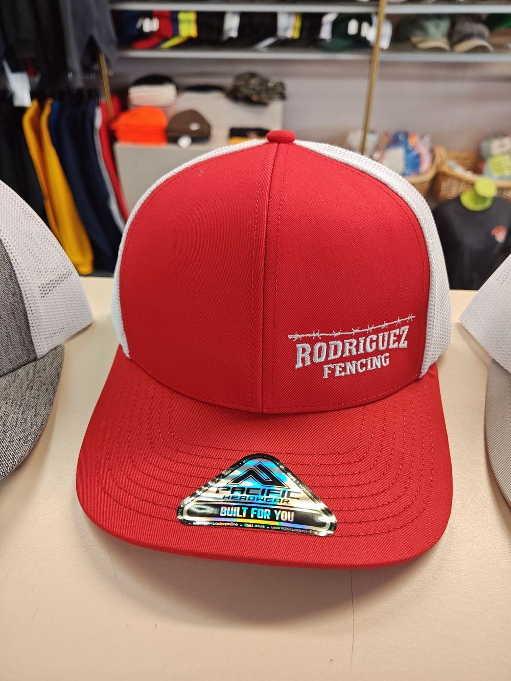 Red trucker cap embroidered in white with the words Rodriguez Fencing
