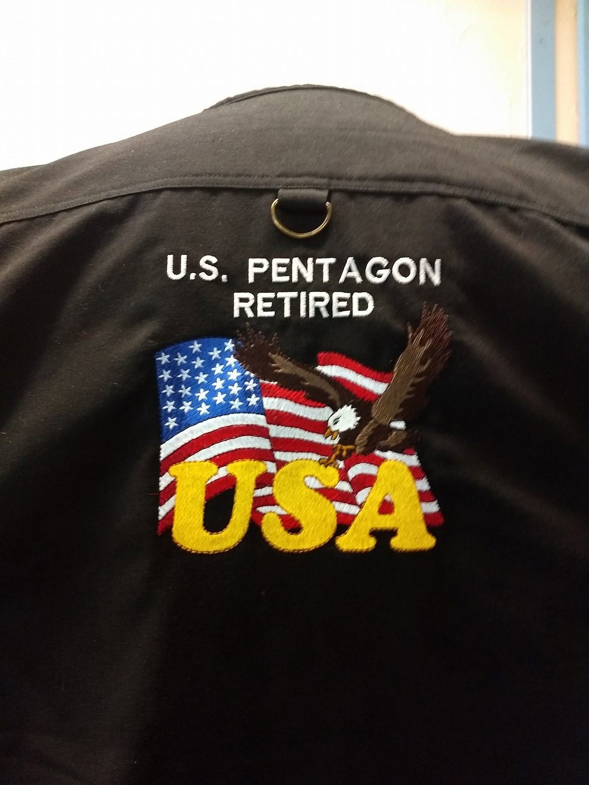 Back of a black jacket embroidered with an American flag, a bald eagle, USA lettering, and U.S. Pentagon Retired