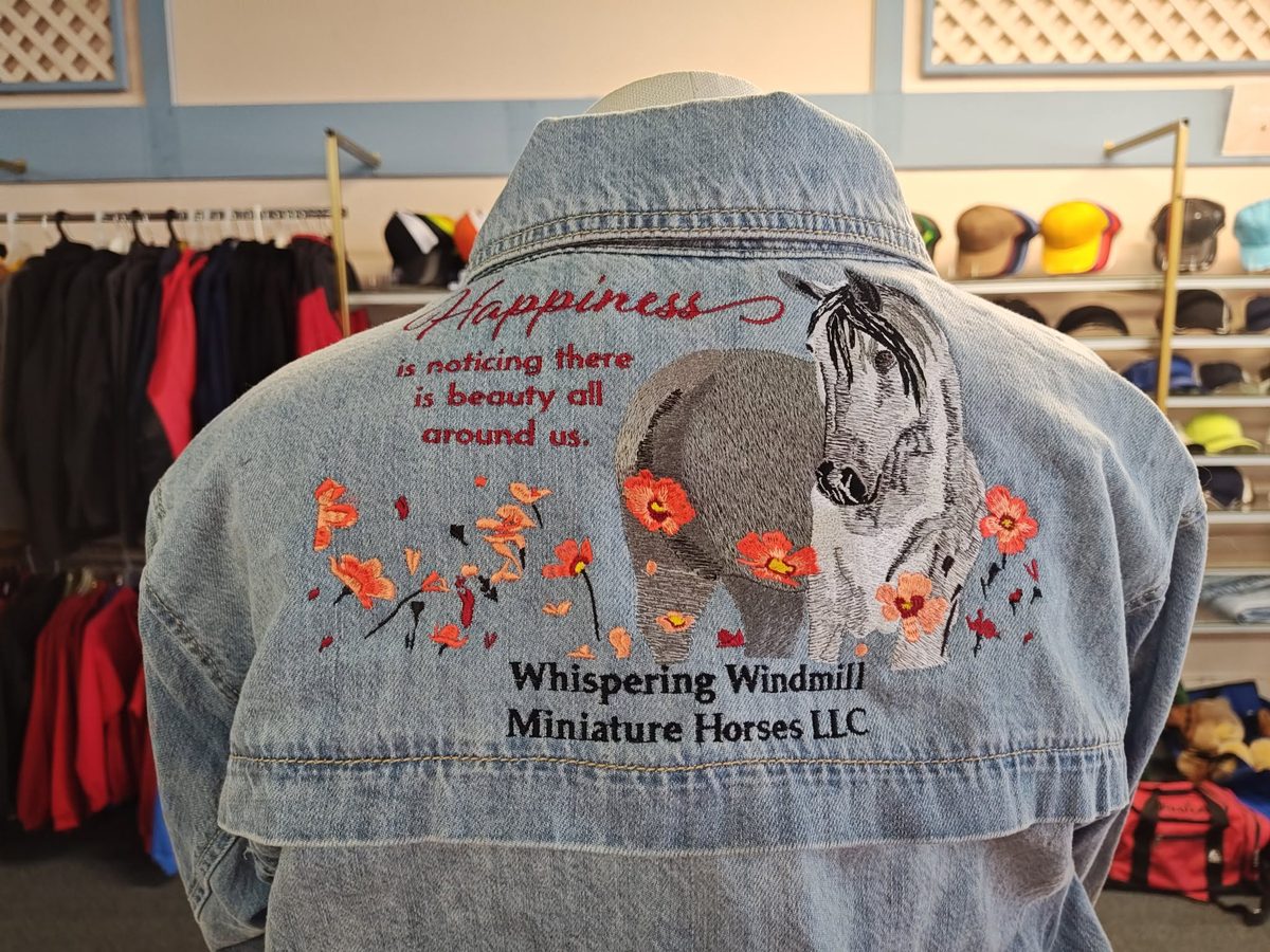 Back of a denim jacket embroidered with a horse, red poppies, and Whispering Windmill lettering